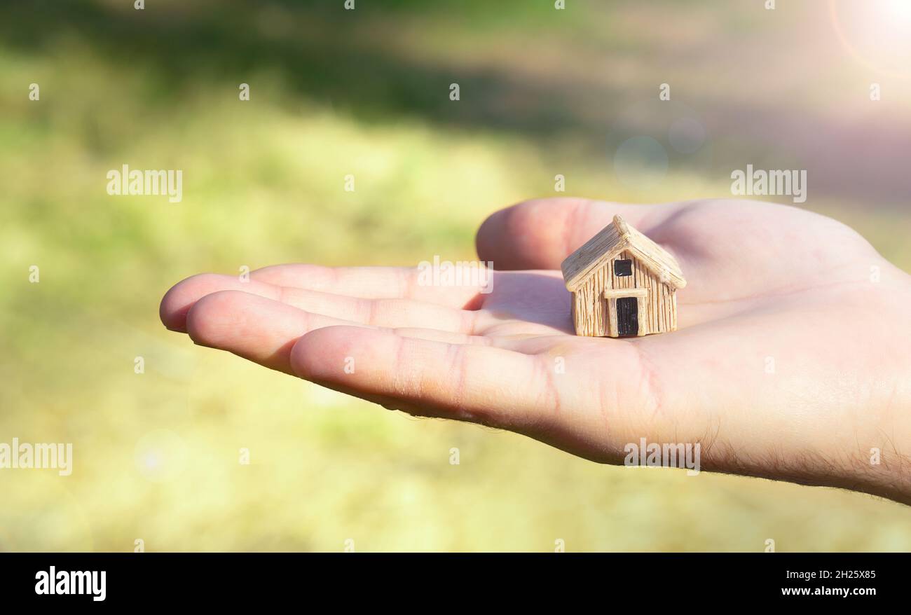 Figurine de maison à la main sur fond d'herbe floue.Concept d'achat éco-maison. Banque D'Images