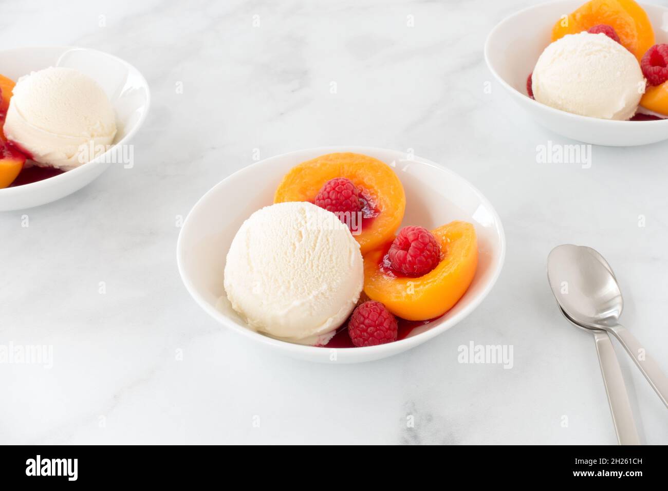 Glace à la vanille avec pêches, framboises et sauce à la framboise dans des bols en marbre blanc avec espace pour les copies.Vue à angle bas. Banque D'Images