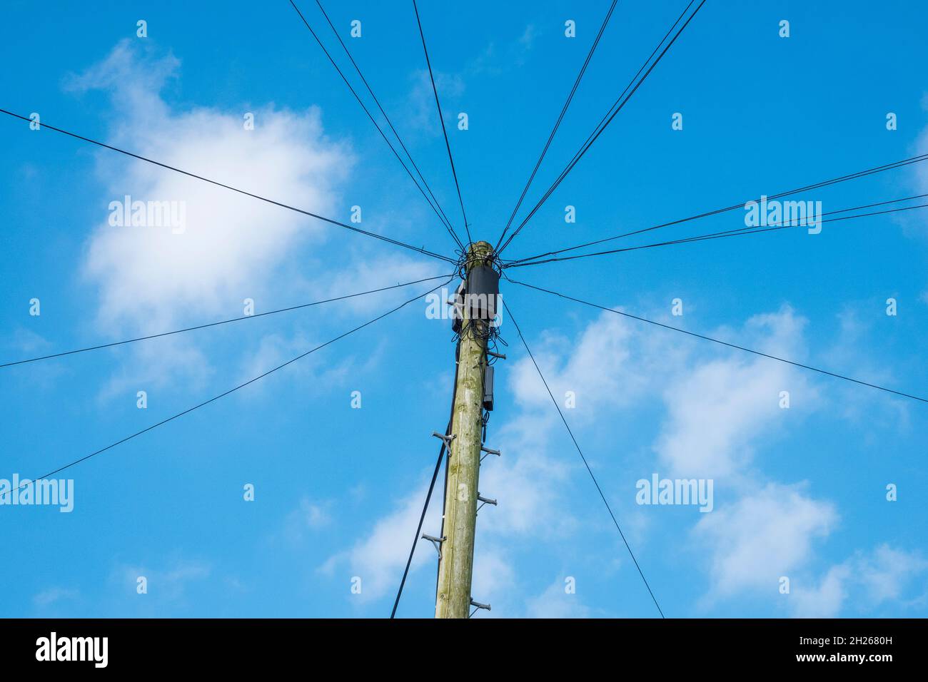 Un poteau de ligne téléphonique contre un ciel bleu avec des câbles rayonnant comme des rayons de roue Banque D'Images