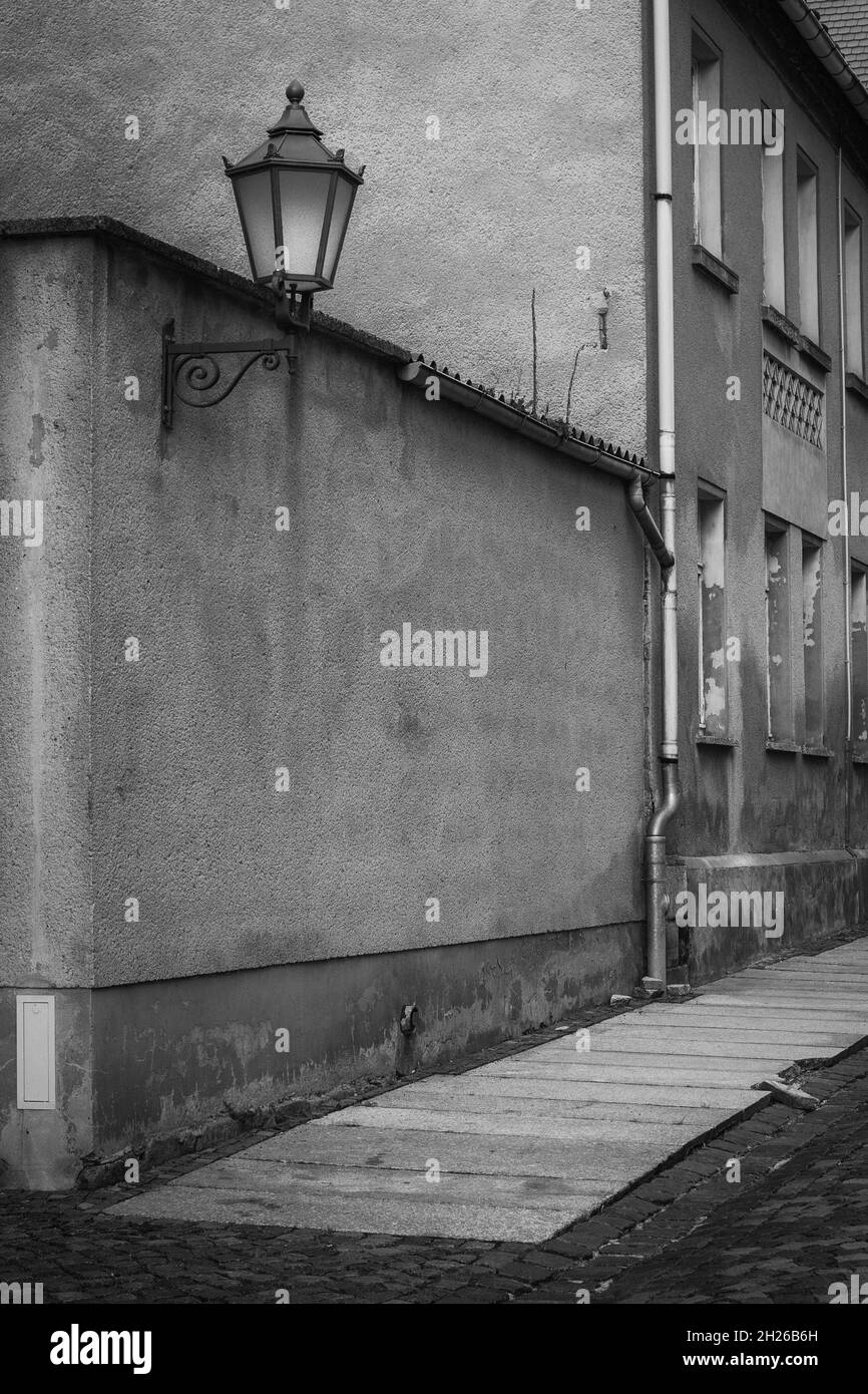 photo en noir et blanc d'une rue qui a besoin d'être rénovée avec un trottoir endommagé et des façades avec une vieille lampe de rue en ruine Banque D'Images
