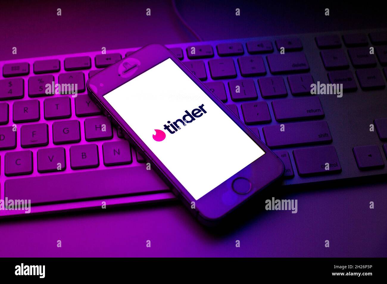 Sur cette photo, un logo Tinder apparaît sur un smartphone, au-dessus du clavier d'un ordinateur. Banque D'Images