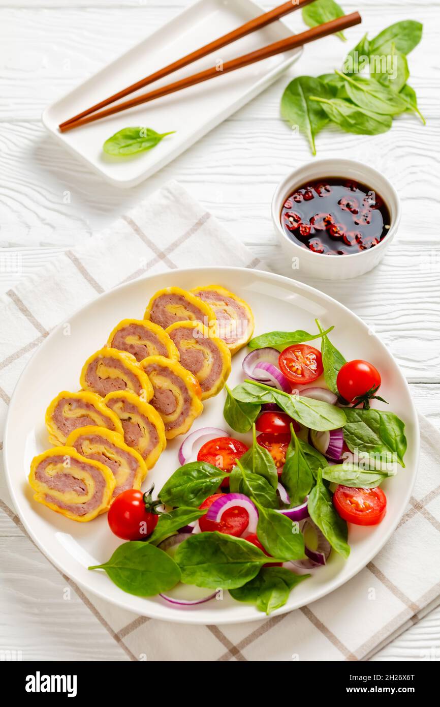petit-déjeuner au jambon et au fromage, omelettes et salade d'oignons rouges aux épinards frais sur une assiette sur une table en bois blanc, vue verticale depuis le dessus, clos Banque D'Images
