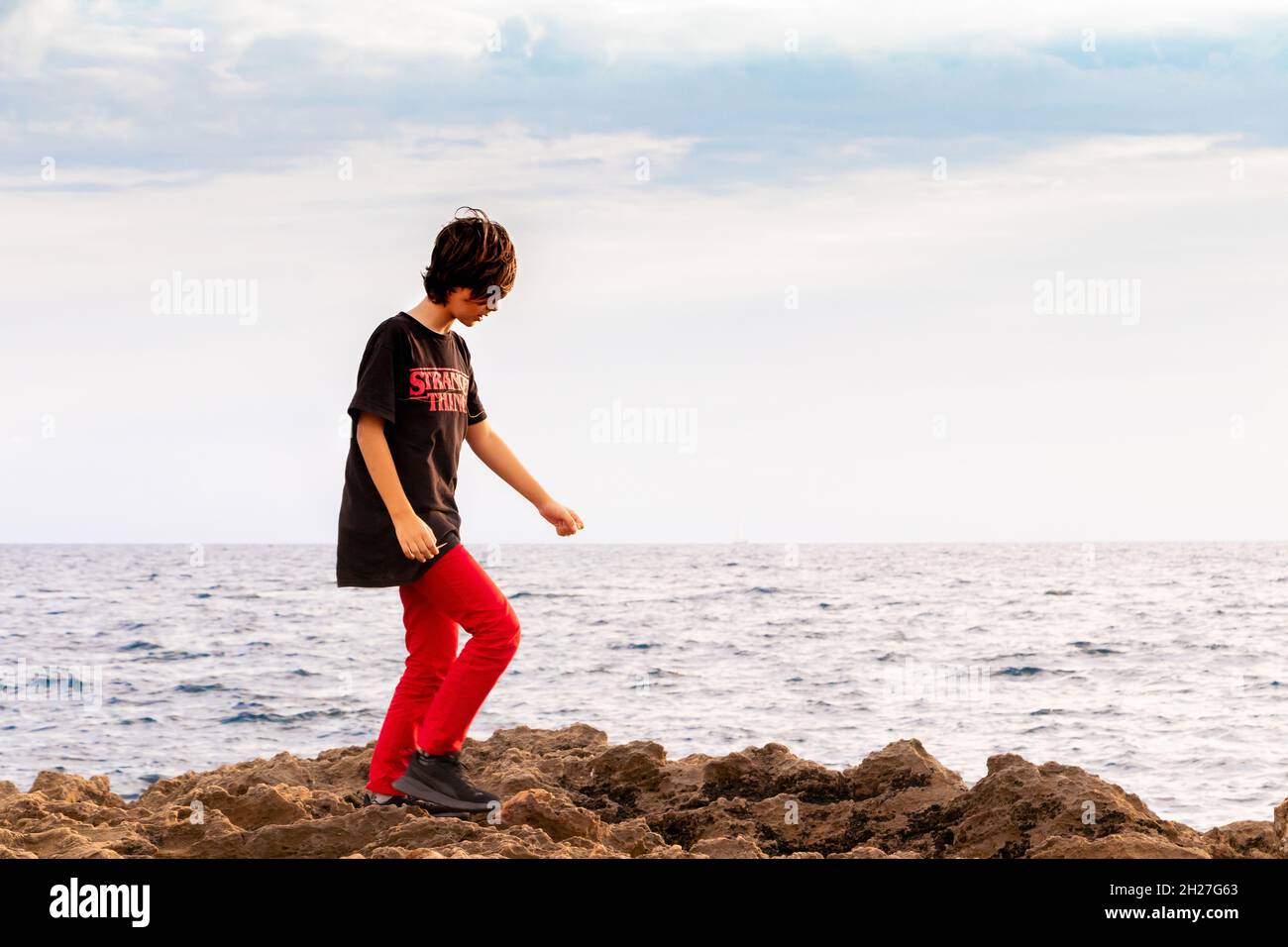 Vue en soirée d'un jeune garçon qui claque sur les rochers au bord de la mer à CAN Pastilla près de Palma Mallorca Espagne Banque D'Images