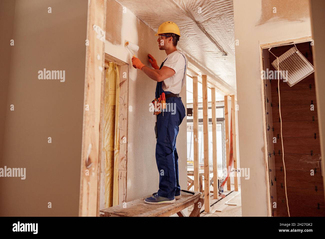 Un homme de construction peint mur dans la maison en construction Banque D'Images