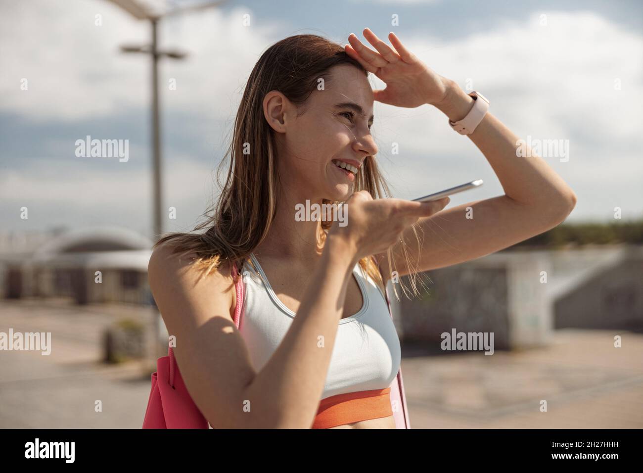 La Sportswoman en haut utilise le mode haut-parleur sur le téléphone en ombrageant ses yeux avec la main sur le front de mer Banque D'Images