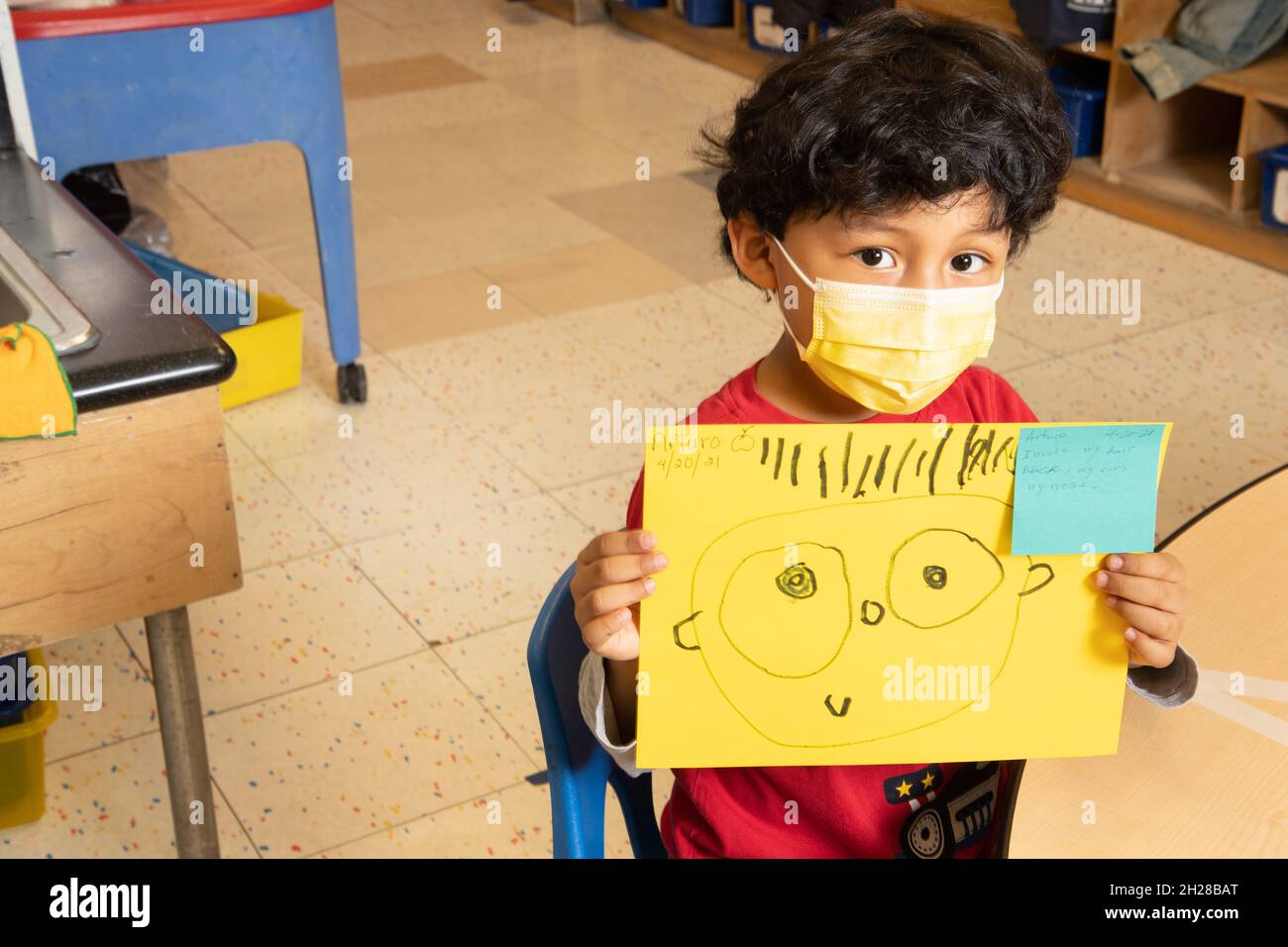 Éducation préscolaire garçon de 4-5 ans tenant le dessin qu'il a fait de la personne, portant un masque facial pour protéger contre l'infection Covid-19 Banque D'Images