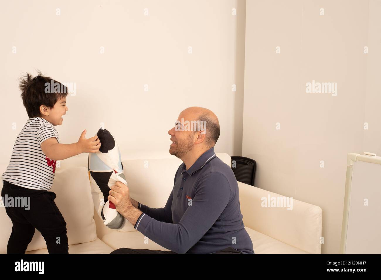Un jeune garçon de deux ans joue un coup de jeune avec son père et son coussin Banque D'Images