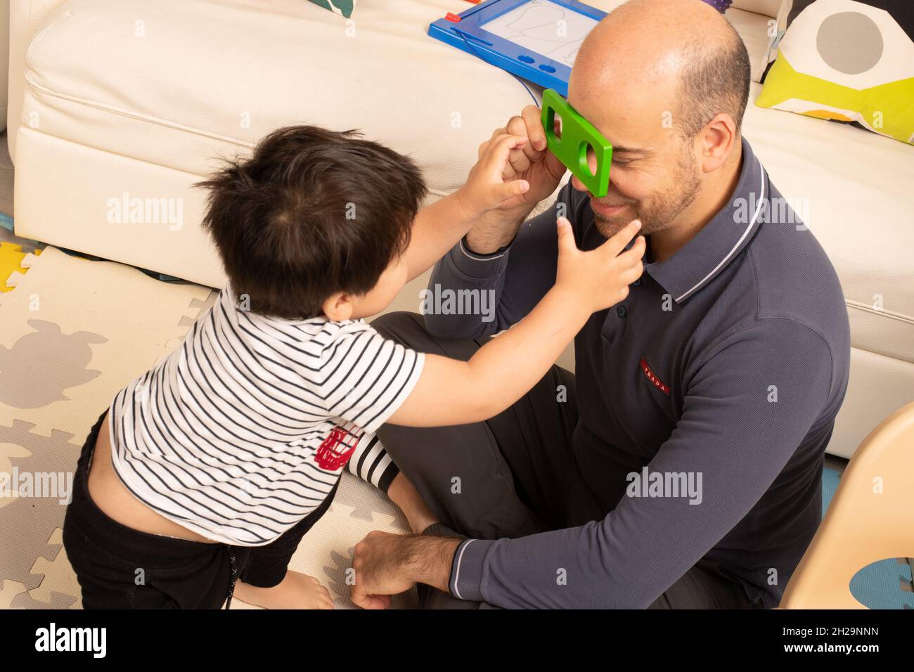 Un tout-petit garçon de deux ans joue avec un père qui tient une pièce de puzzle et la traverse Banque D'Images