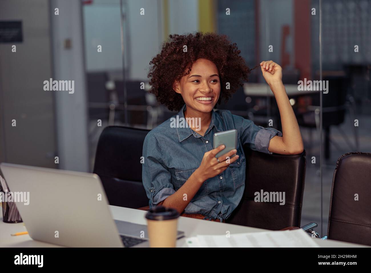 Une jolie femme souriante utilisant un téléphone portable sur son lieu de travail Banque D'Images