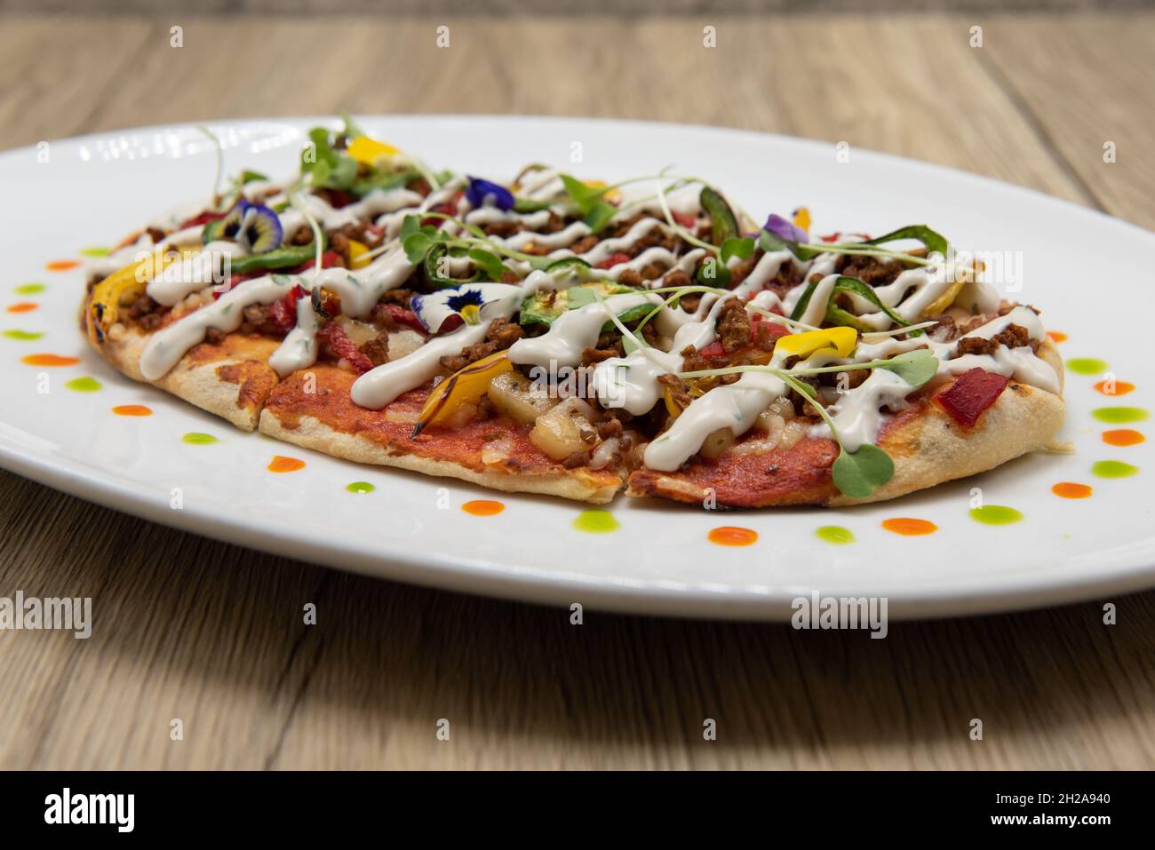 Pizza à pain plat ovale sur une assiette décorée avec des garnitures de légumes saines et une croûte mince. Banque D'Images