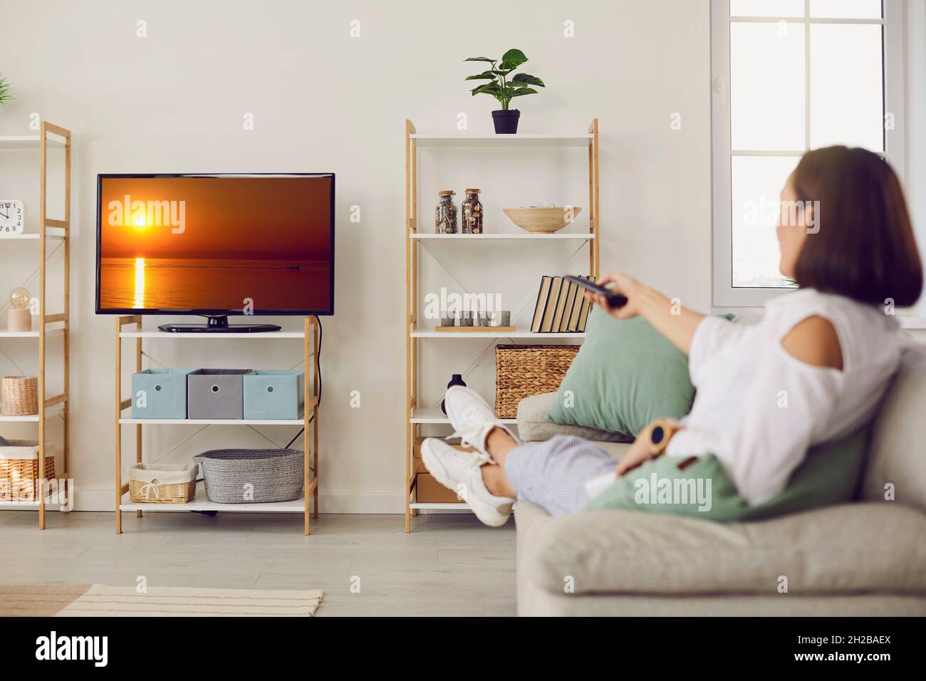 Femme assise sur un canapé à la maison et regardant un film sur un téléviseur avec grand écran HD Banque D'Images