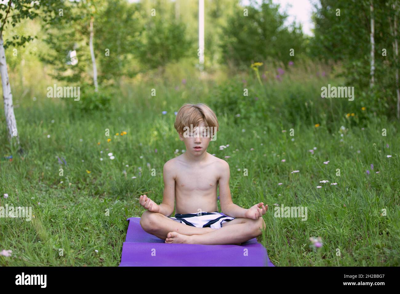 jeune garçon d'âge préscolaire méditant pendant un cours de yoga à l'extérieur du parc en été Banque D'Images