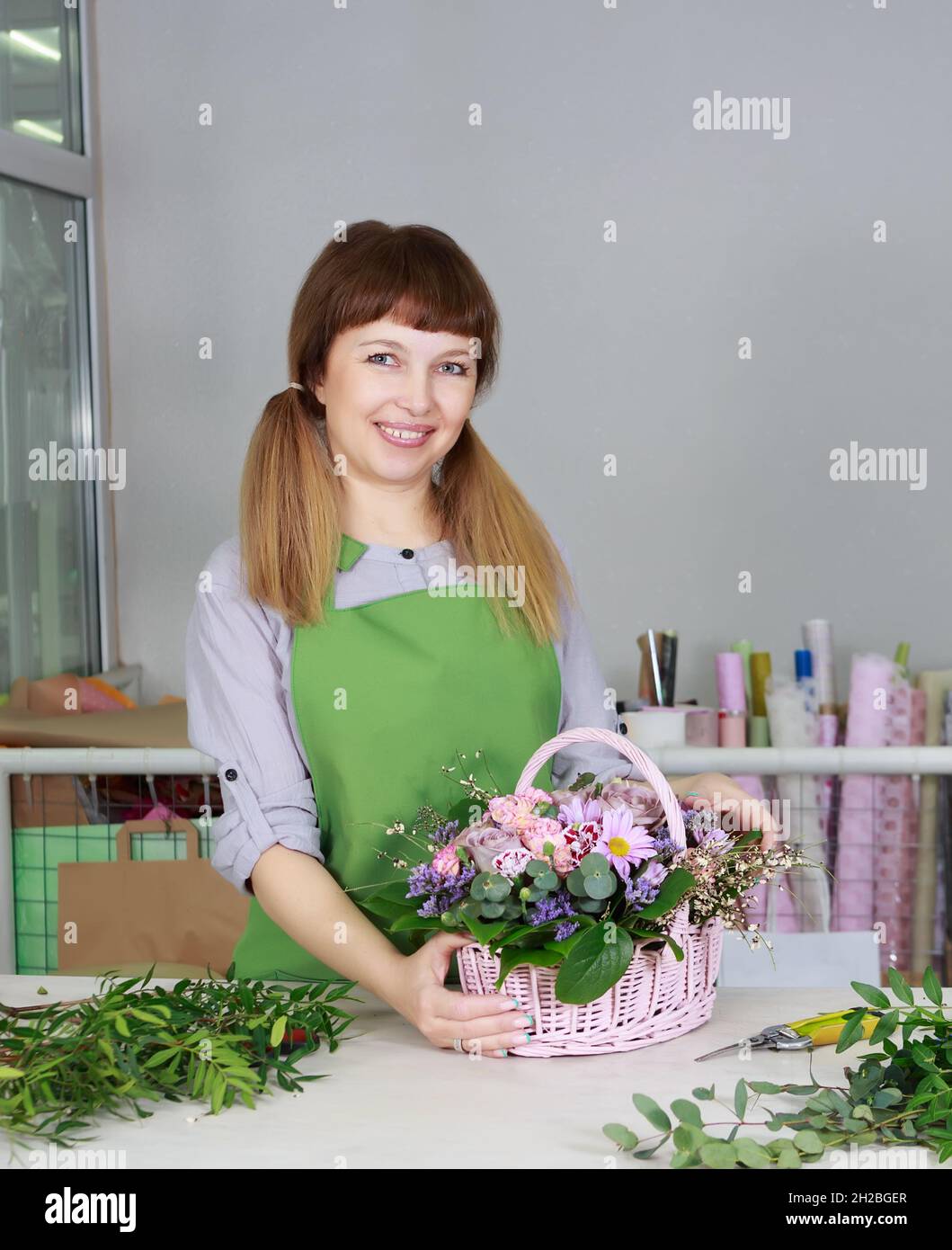 Portrait d'une femme fleuriste souriante et heureuse tenant un bouquet de fleurs dans le panier d'un fleuriste.Concept d'affaires, de vente ou de fleurs. Banque D'Images