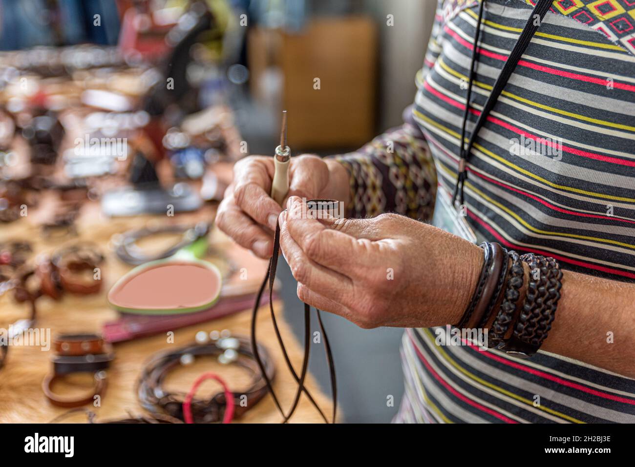 Gros plan des mains d'un artisan qui fait des bracelets avec du cuir dans son atelier Banque D'Images