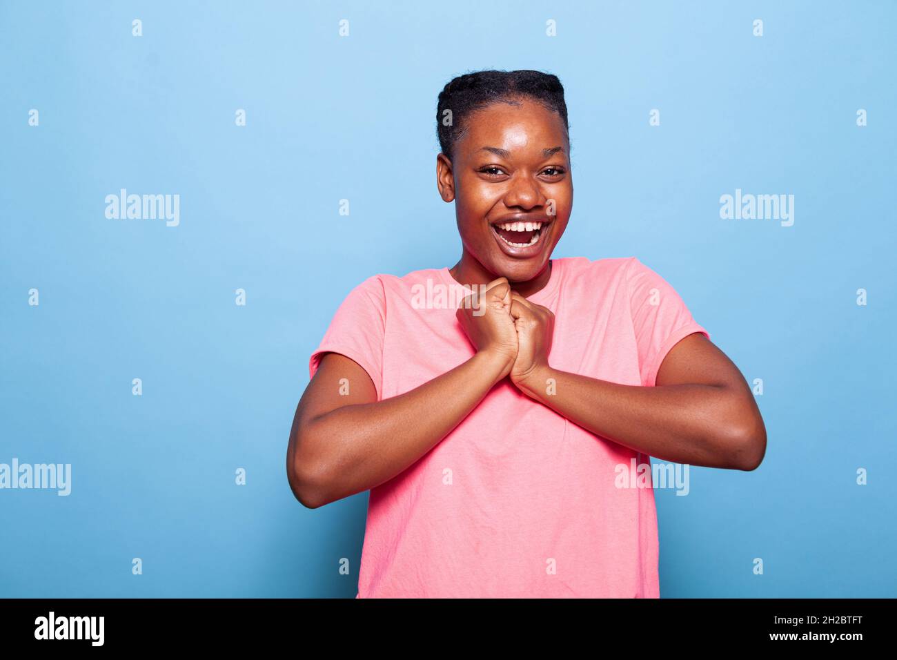 Portrait d'un adolescent afro-américain émerveillé souriant à l'appareil photo pour une expression faciale heureuse après avoir raconté de bonnes nouvelles en appréciant la photographie en studio avec un fond bleu.Concept de célébration Banque D'Images