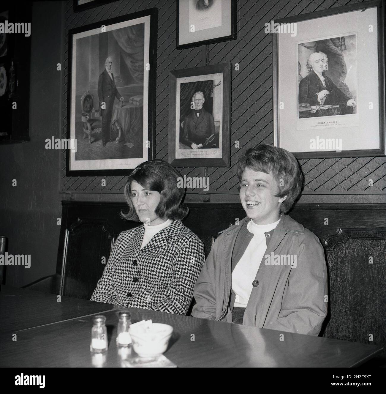 Années 1960, historique, deux jeunes dames assis dans un dîner ou un restaurant, Virginia, Etats-Unis.Derrière eux, sur un mur, encadrés des images de personnalités américaines historiques célèbres, dont l'un de John Adams, un père fondateur du pays et son second président de 1797 à 1801. Banque D'Images