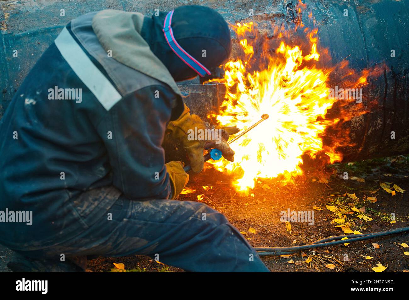 Le soudeur se trouve près du tuyau et le coupe à l'aide du soudage au cétylène.Un travailleur dans la rue coupe des tuyaux de grand diamètre et des étincelles et des mouches de feu Banque D'Images