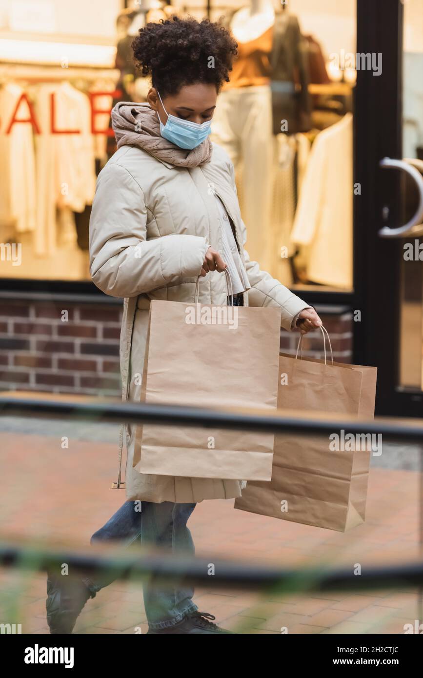 brunette afro-américaine femme dans un masque médical tenant des sacs de shopping dans le centre commercial Banque D'Images