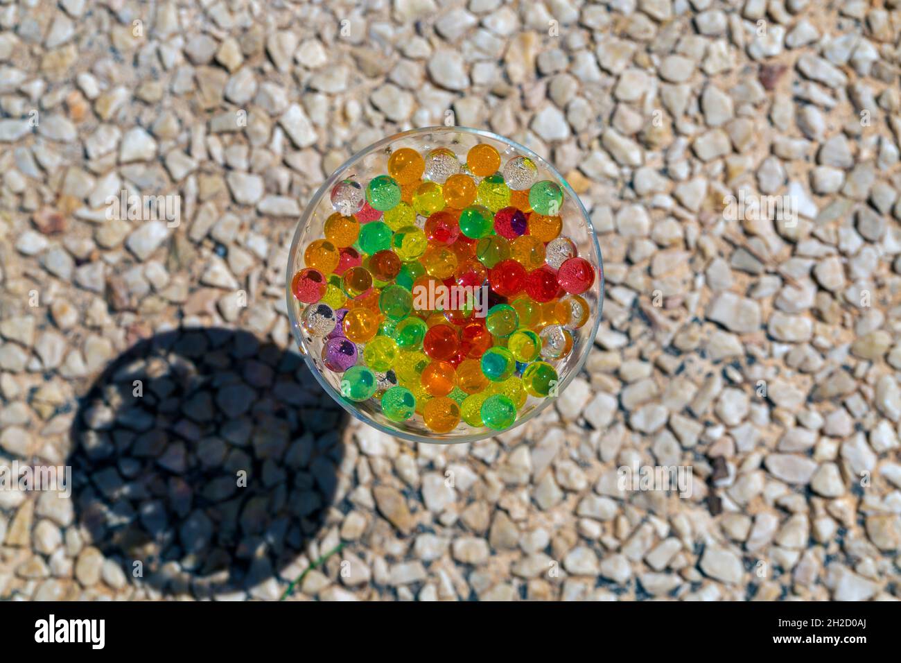 photo d'une tasse en verre placée sur un sol en galets, remplie de perles de couleur (orbis) avec mise au point sélective Banque D'Images
