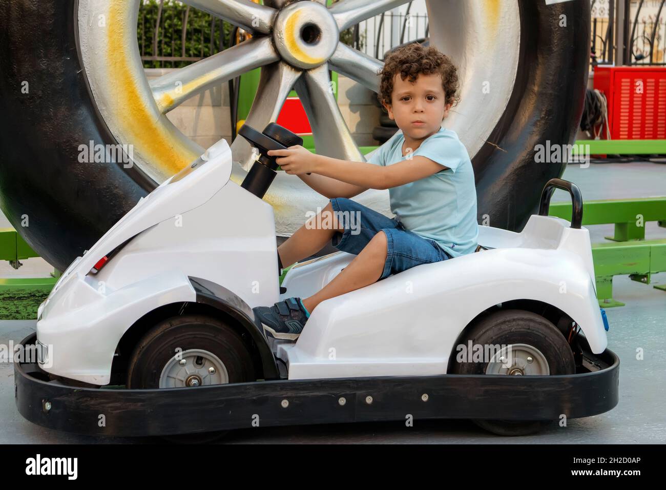 beau garçon caucasien aux cheveux bouclés assis dans une voiture électrique, regardant la caméra Banque D'Images