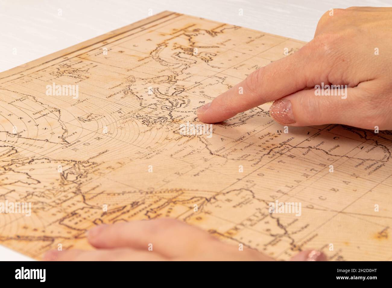 main femelle montre le lieu de voyage sur la carte du monde sur le fond d'une table en bois blanc. gros plan. mise au point sélective Banque D'Images