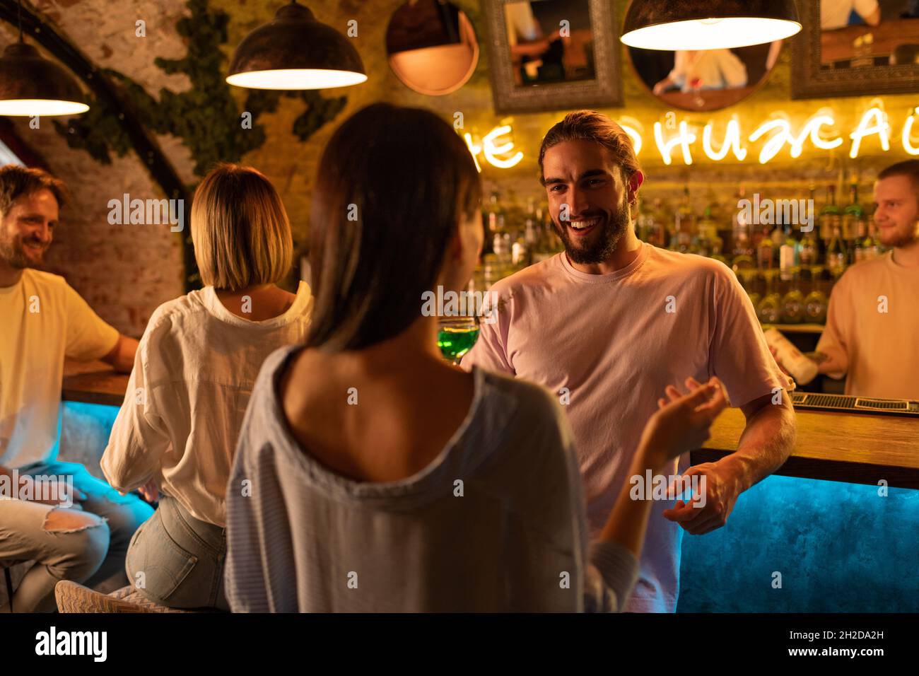Homme barbu riant à blague de femme tout en passant du temps avec un ami au pub la nuit Banque D'Images