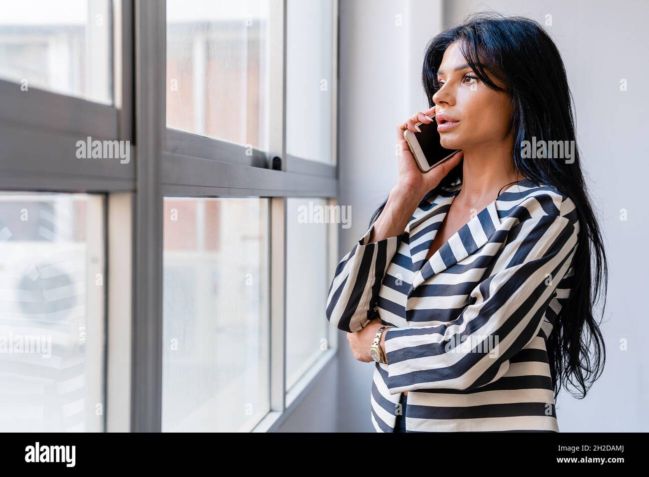 Femme élégante parlant sur un smartphone près de la fenêtre Banque D'Images