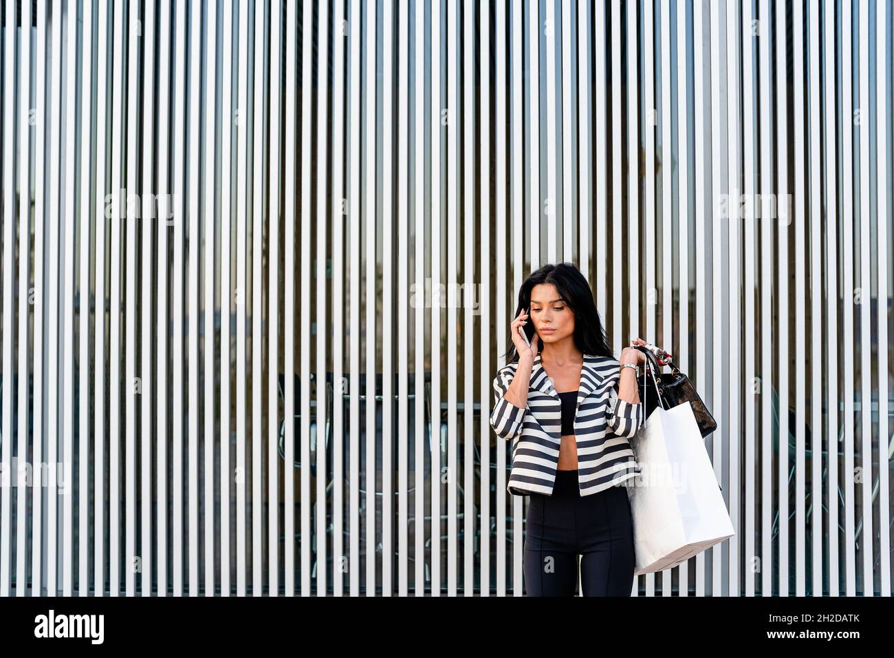 Femme élégante parlant sur un smartphone près d'un mur d'architecture moderne Banque D'Images