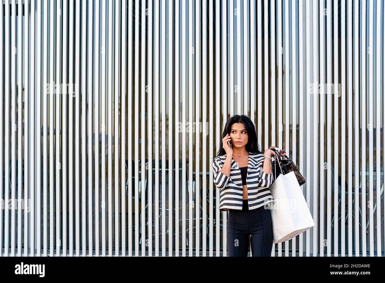 Femme élégante parlant sur un smartphone près d'un mur d'architecture moderne Banque D'Images