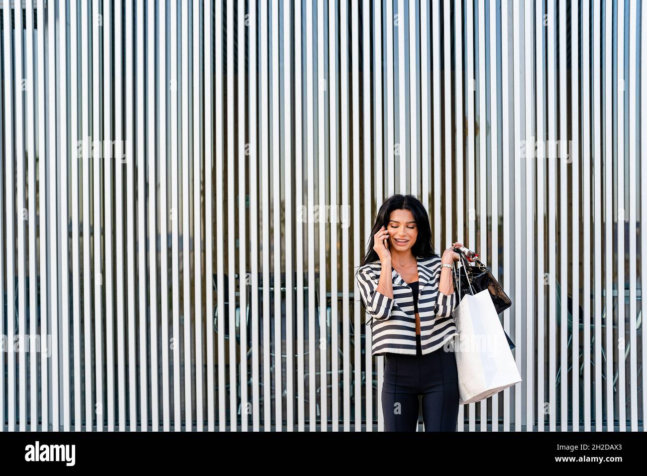 Femme élégante parlant sur un smartphone près d'un mur d'architecture moderne Banque D'Images
