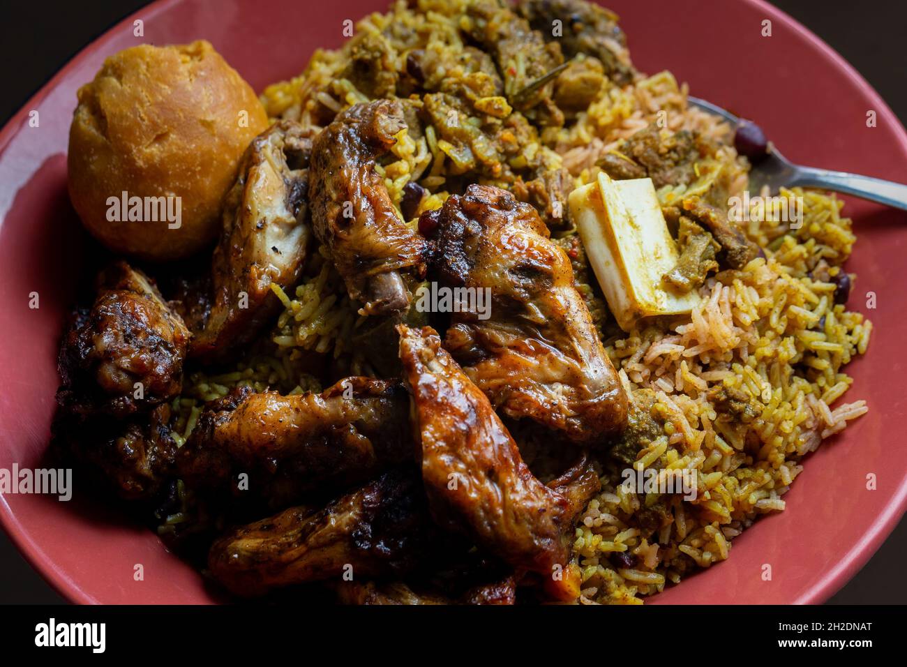 Ailes de poulet jamaïcaines traditionnelles, chèvre au curry et boulettes frites avec riz et petits pois Banque D'Images