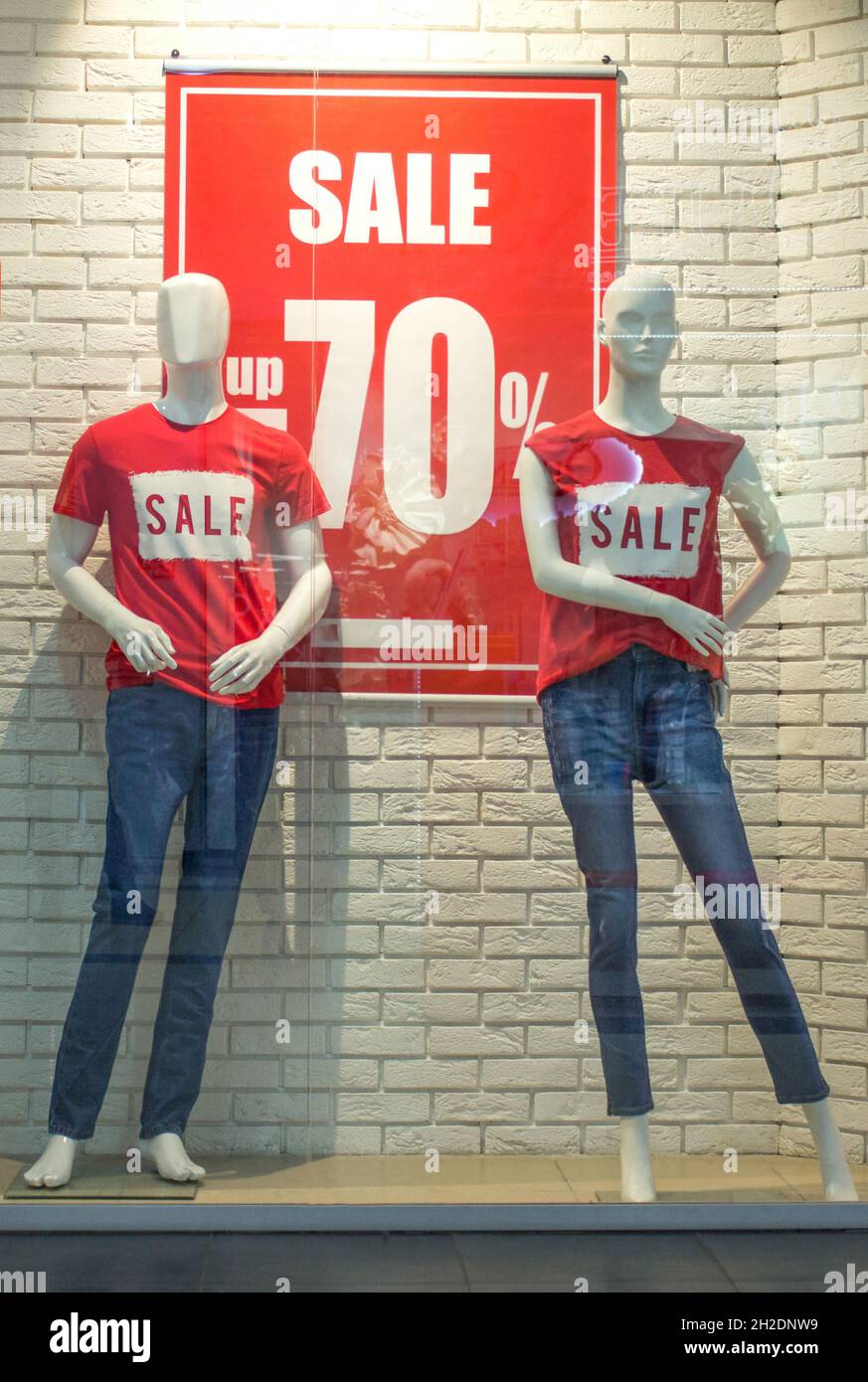 Les mannequins féminins en T-shirts rouges et jeans bleus dans une fenêtre du magasin sur un fond de mur de briques blanches.Remise promotionnelle de 70 %.Noir ven Banque D'Images