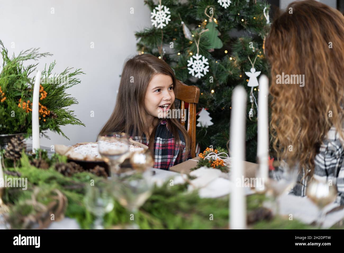 La mère et la fille de la famille ont le petit déjeuner dans le salon pour Noël à une grande table décorée de bougies de sapin.Femme donnant un cadeau à un enfant Banque D'Images