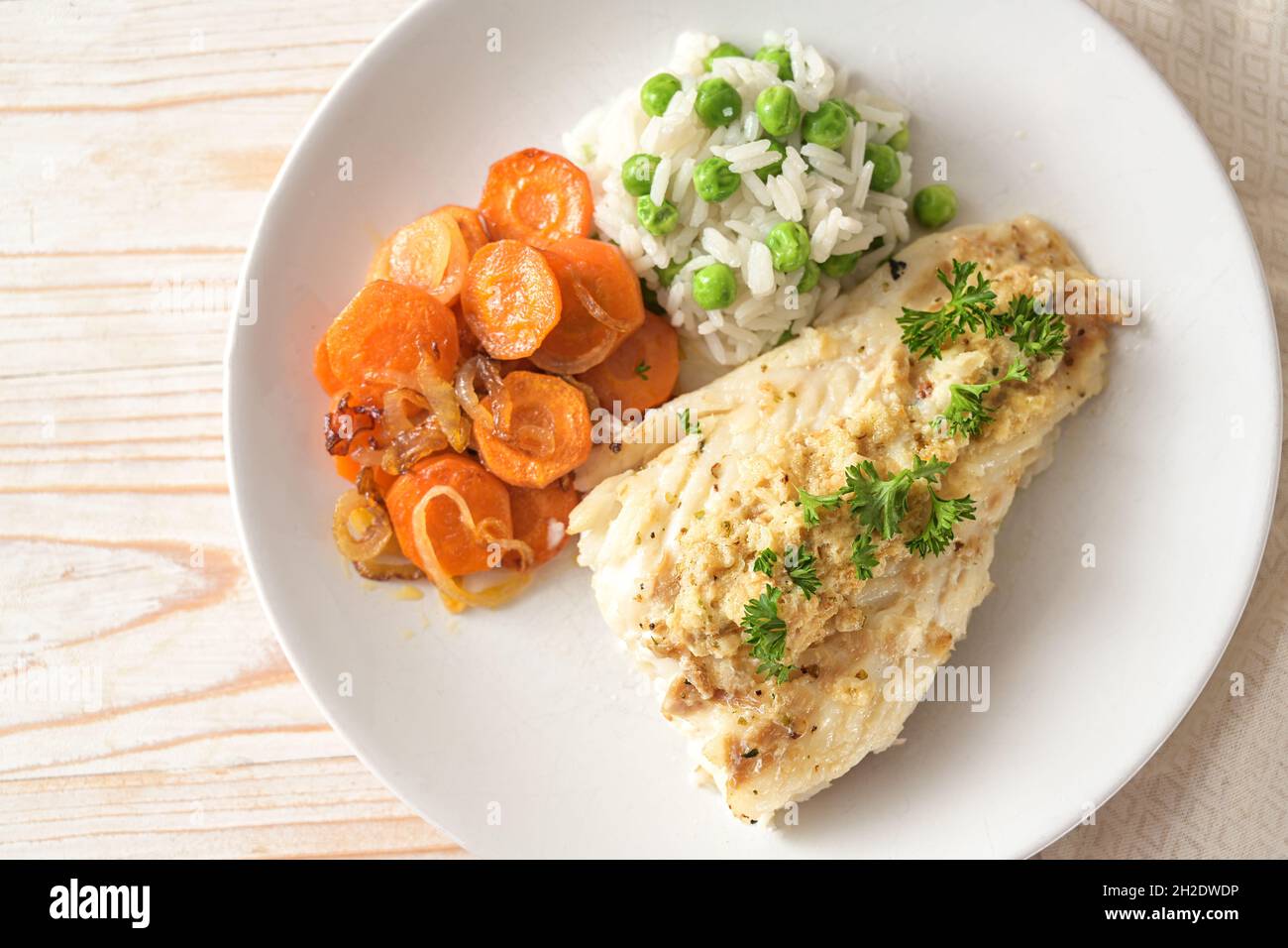 Repas de poisson sain à partir de filet de morue avec garniture épicée et persil, carottes et riz aux pois verts sur une assiette blanche, vue d'en haut, sel Banque D'Images