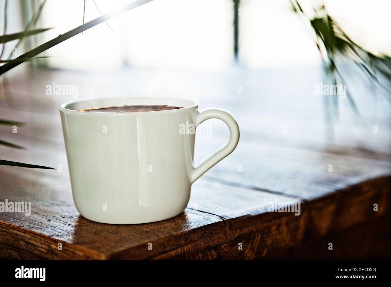 Tasse à café en céramique/porcelaine blanche sur table en bois, rétroéclairée avec le soleil derrière Banque D'Images
