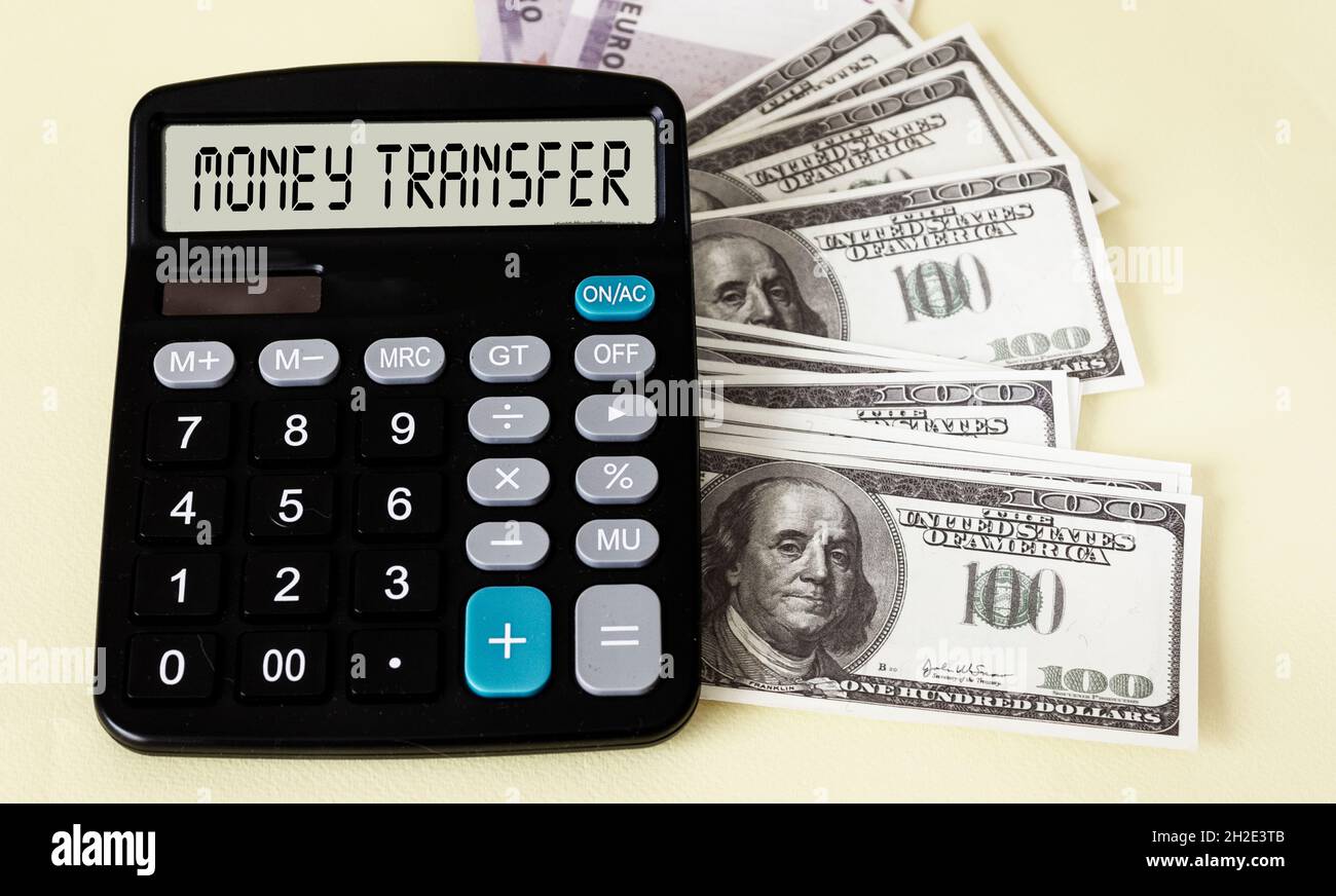 Calculatrice avec texte sur l'écran TRANSFERT D'ARGENT, à côté des billets de dollars et d'euros sur fond jaune. Banque D'Images