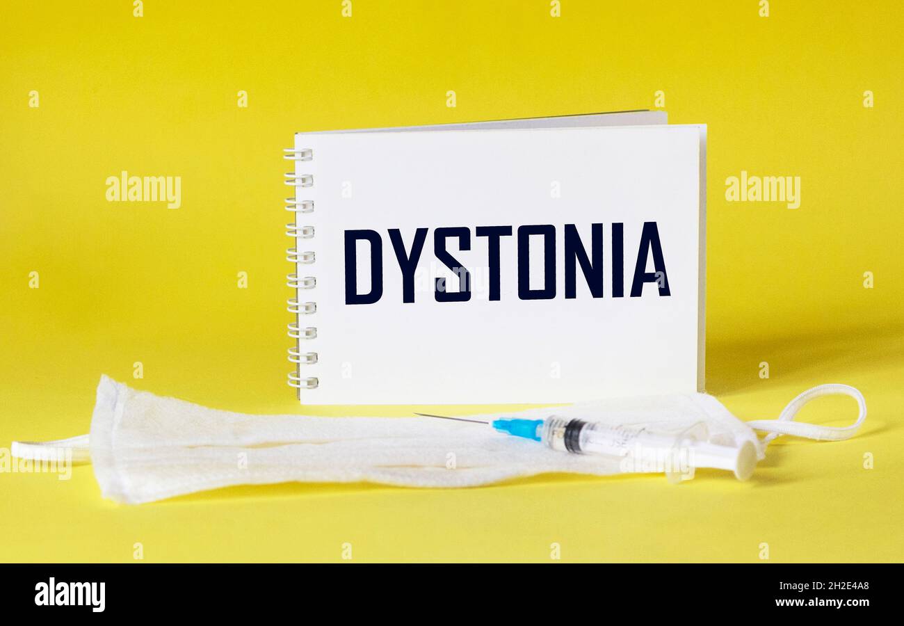 Dystonie - le diagnostic est écrit sur un papier blanc.Seringue et masque médical sur fond jaune Banque D'Images