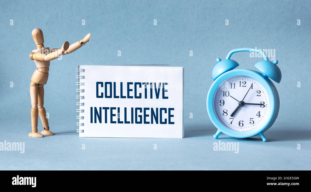 Sur fond bleu, un carnet avec le texte INTELLIGENCE COLLECTIVE, à côté d'une poupée en bois et d'un réveil Banque D'Images