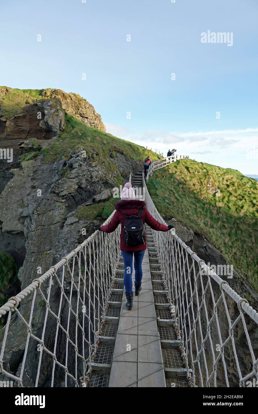 Une jeune fille touristique traverse le pont de corde de Carrick-a-rede, une attraction touristique populaire en Irlande du Nord.Ballintoy, Comté d'Antrim, Irlande du Nord 18.11.2019 Banque D'Images