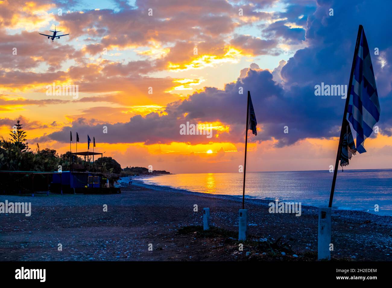 Drapeaux devant le plus beau coucher de soleil doré et avion à l'horizon sur Ialysos Beach sur l'île de Rhodes Grèce. Banque D'Images