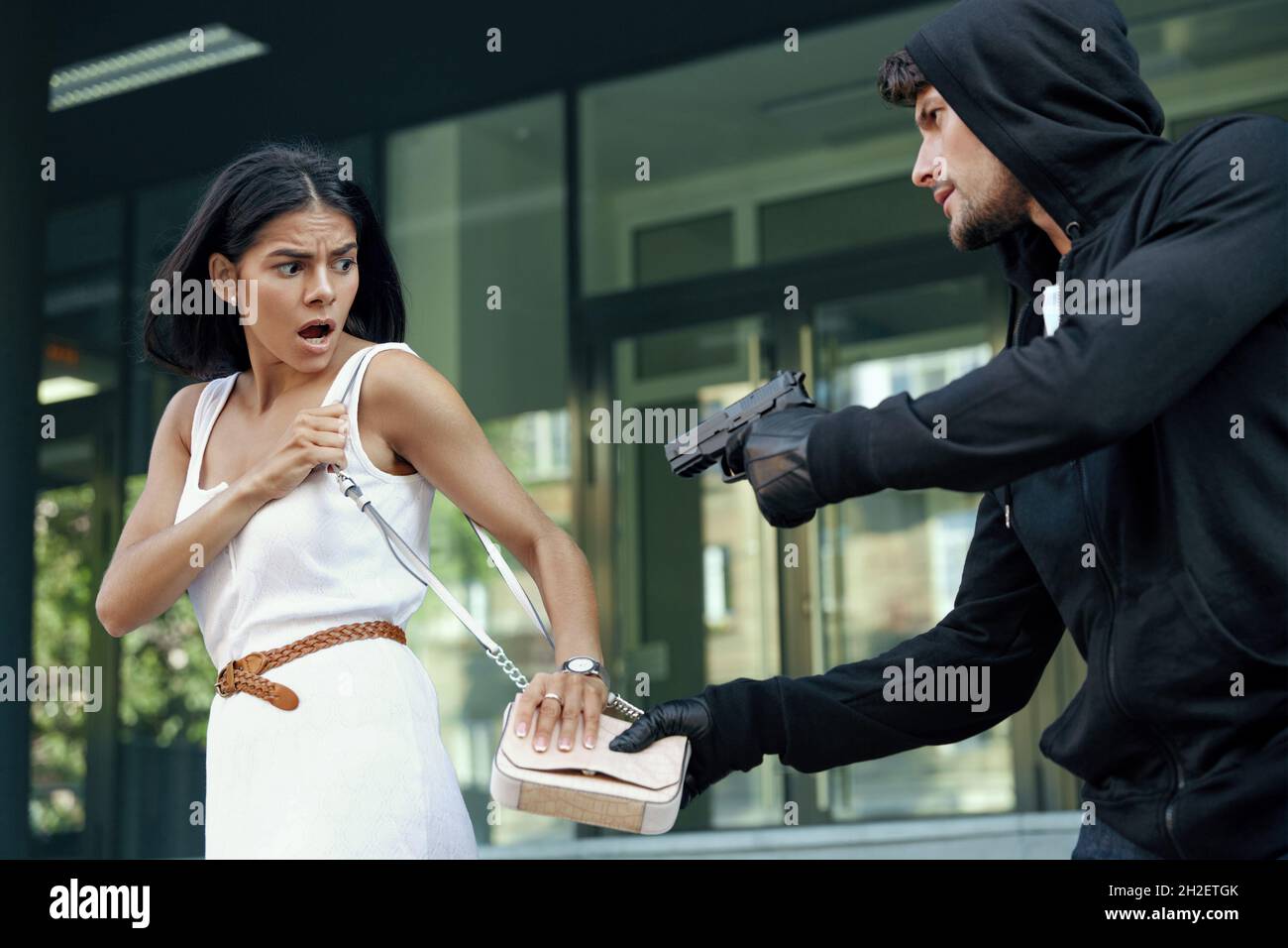 Un voleur agressif veut voler le sac à main d'une fille effrayée. Homme  menaçant avec le pistolet et veulent punch jeune femme européenne. Homme  bandit porter noir ho Photo Stock - Alamy