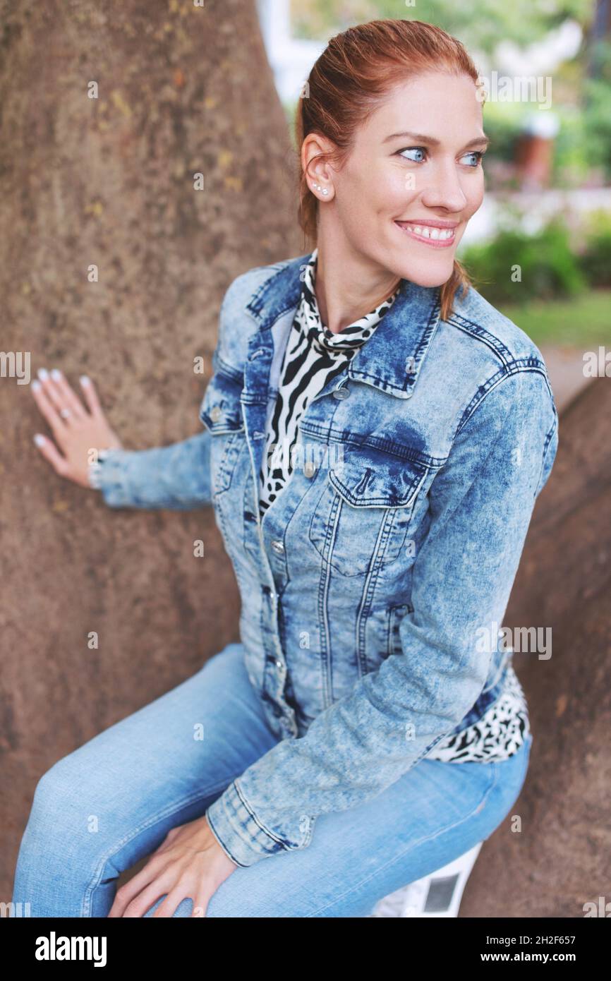 Jeune positive naturel redhead beauté femme torrente sourire, regardant loin, assis sur la branche de l'arbre Banque D'Images