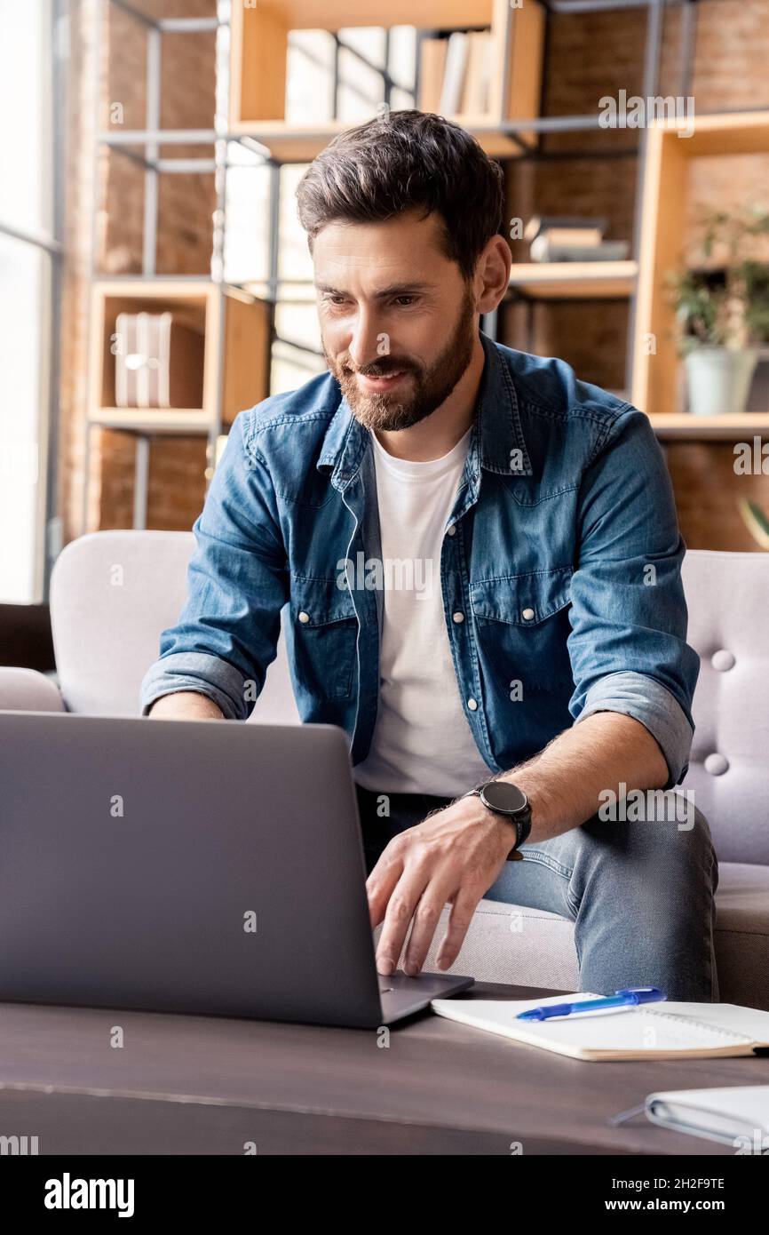Homme souriant travaillant sur un ordinateur portable, consultant des e-mails, écrivant des messages sur les réseaux sociaux Banque D'Images