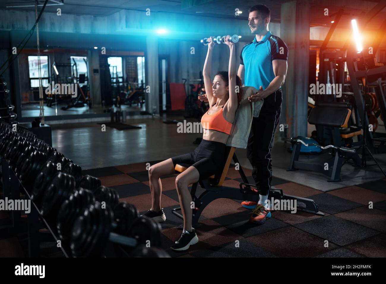 jeune femme s'entraînant dans la salle de gym avec haltères et entraîneur sportif personnel Banque D'Images