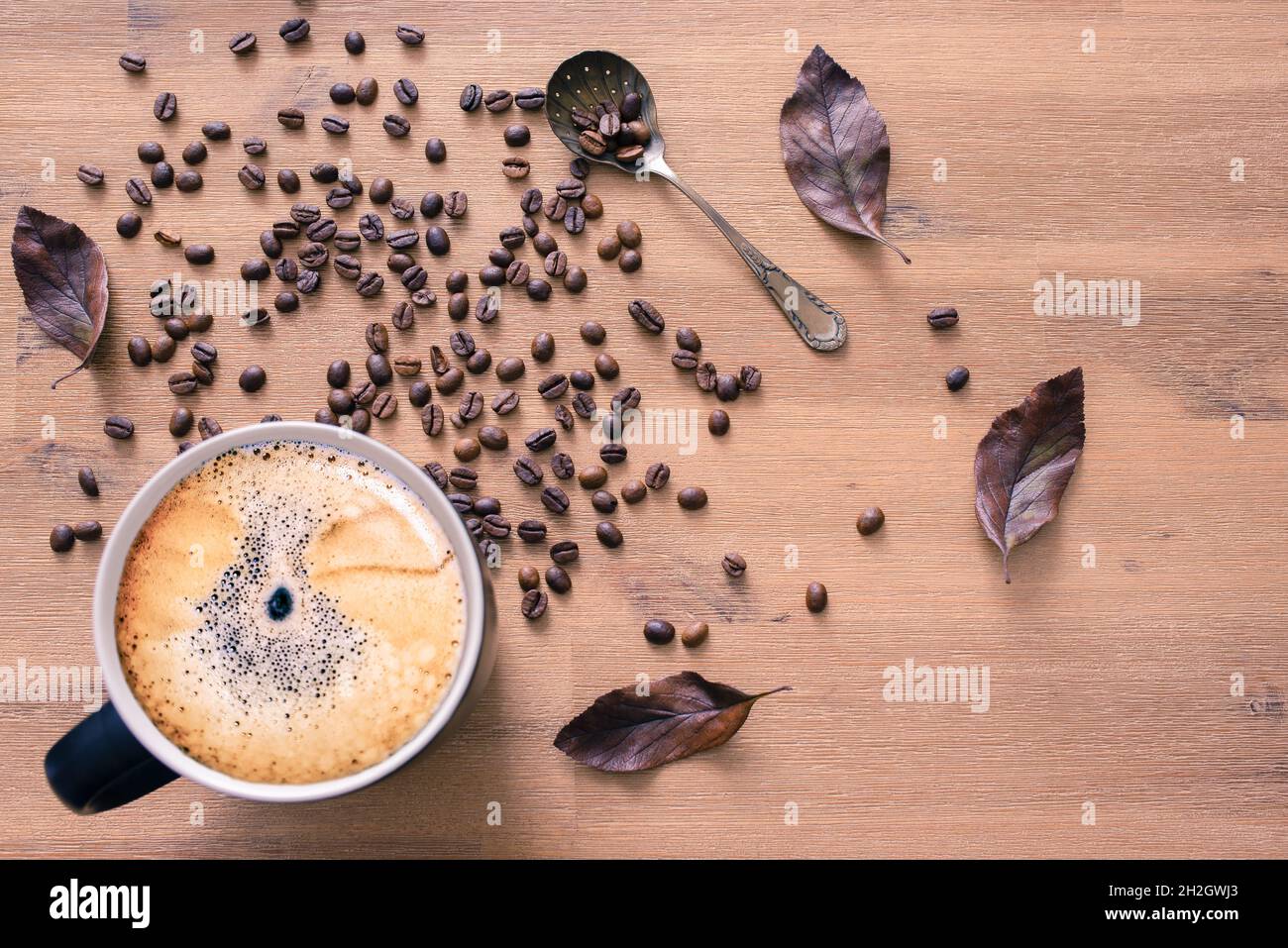 Vue de dessus d'une tasse à café sur fond de table en bois avec grains de café et feuilles brunes. Banque D'Images
