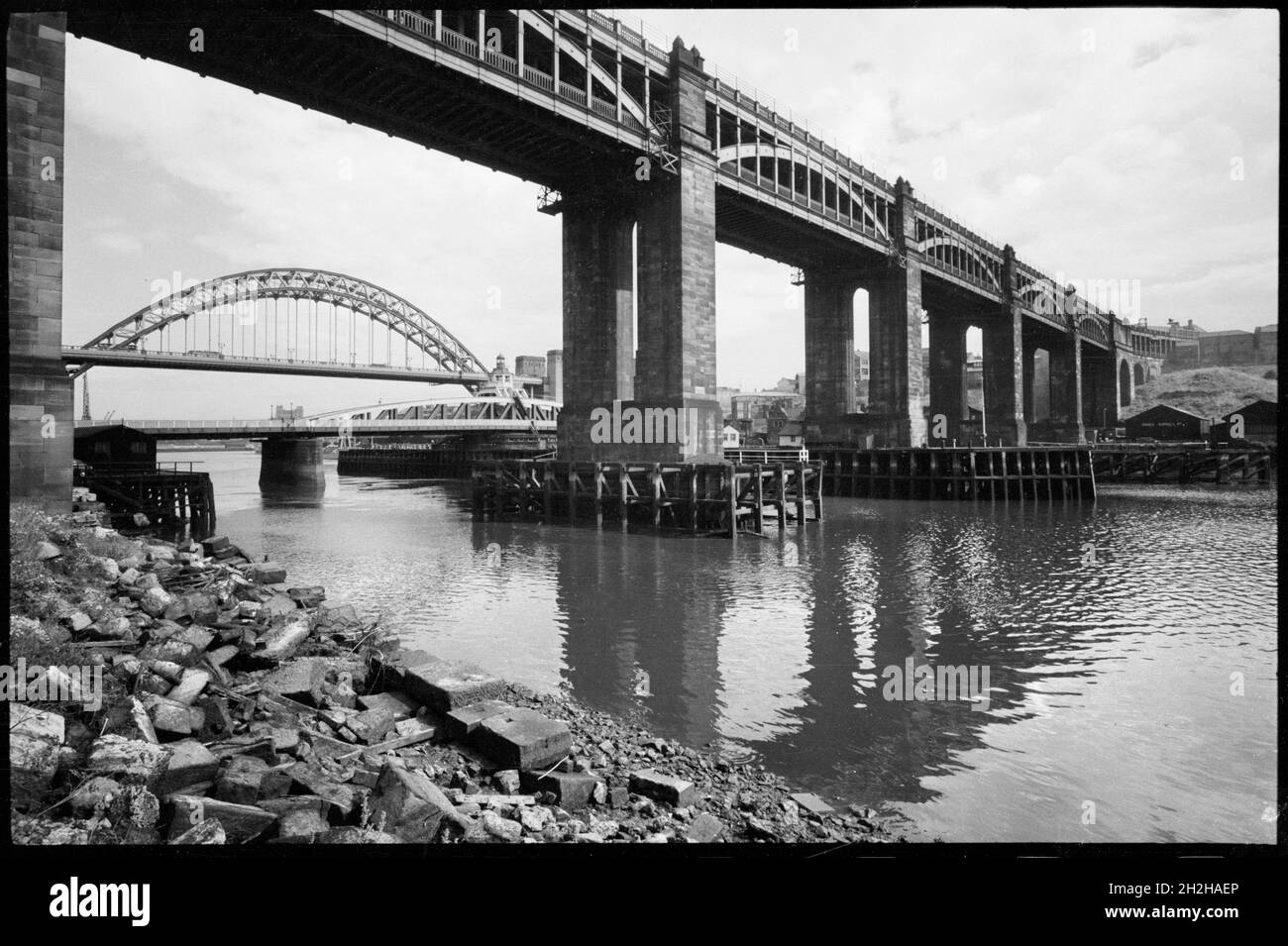 High Level Bridge, Newcastle upon Tyne, c1955-c1980.Vue générale de la rive nord de la rivière Tyne, montrant le pont de haut niveau au premier plan et le pont Swing et le pont de nouveau Tyne en arrière-plan, vus de l'ouest.Le pont de haut niveau est un pont ferroviaire et routier combiné achevé en 1849.La chaussée est sur la poutre inférieure, et les chemins de fer au-dessus, soutenus par six arches segmentaires de fonte, et cinq jetées en pierre.Les deux niveaux ont des parapet ouverts, et le côté sud du pont se compose d'un quai ashlar qui s'étend vers la rivière.La rotation la plus courte se trouve à gauche Banque D'Images