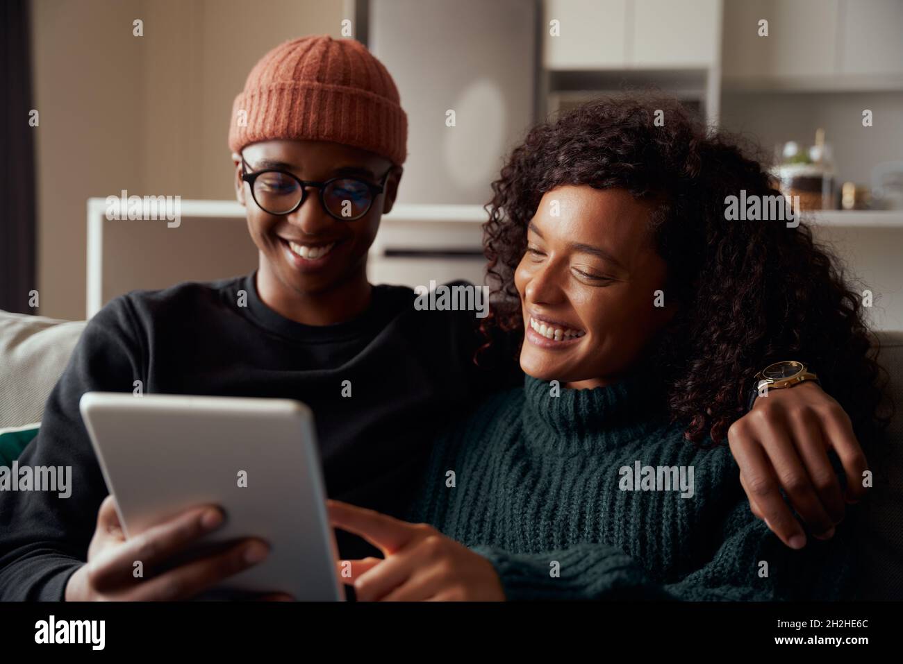 Couple d'adultes branché, multi-ethnique, souriant à la tablette sur le canapé dans l'appartement moderne Banque D'Images