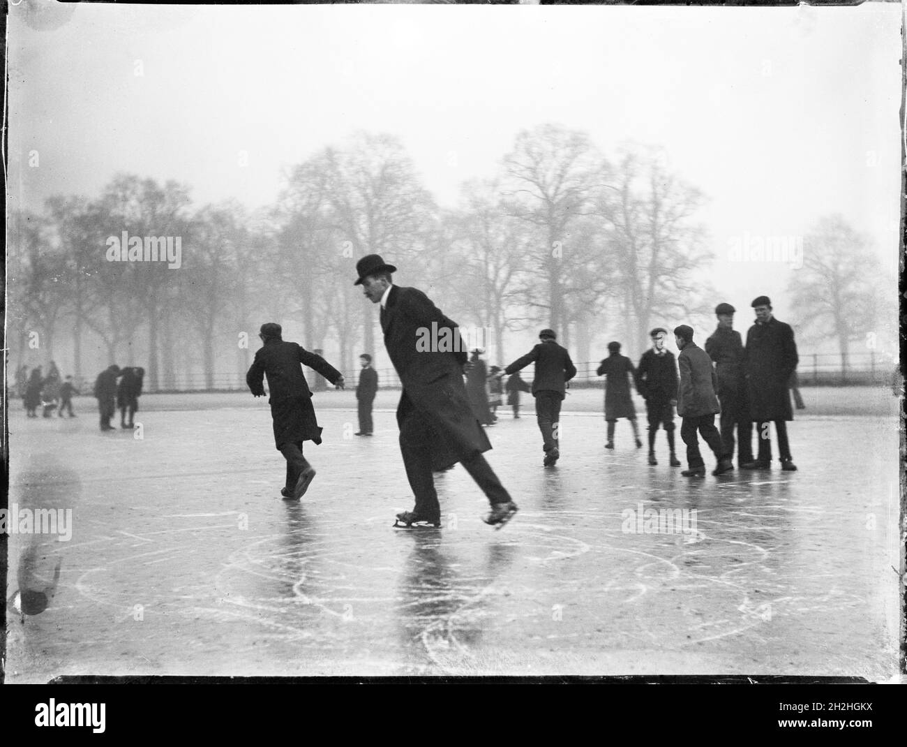 Kensington Gardens, Hyde Park, Cité de Westminster, Greater London Authority, 1903.Un homme de patinage artistique dans les jardins de Kensington avec des garçons regardant en arrière-plan. Banque D'Images