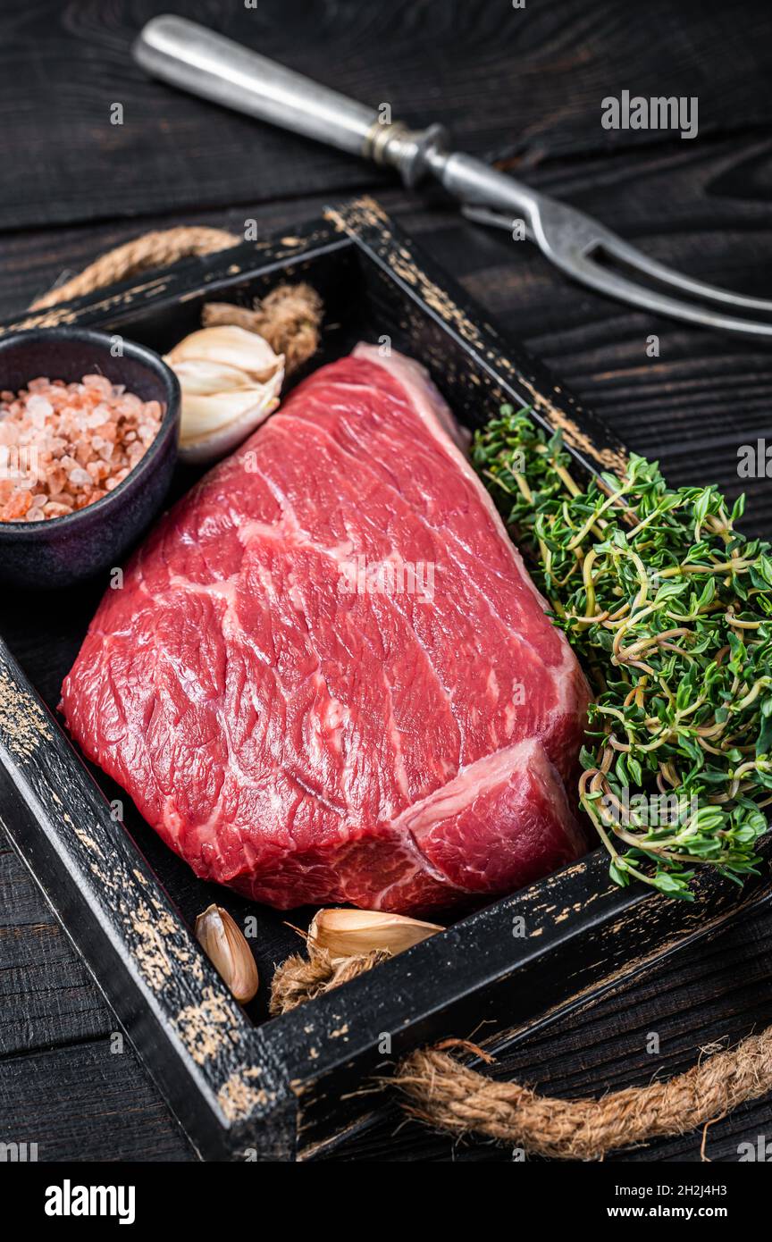 Steak de viande de bœuf coupé au sommet de la sirloine crue ou Picanha dans un plateau en bois avec des herbes. Arrière-plan en bois noir. Vue de dessus Banque D'Images