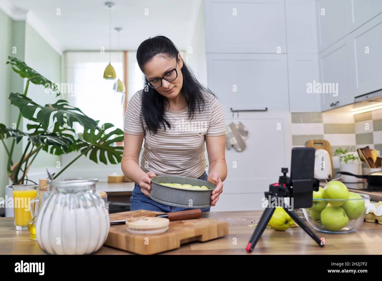 Femme préparant une tarte aux pommes à la maison dans la cuisine, avec un smartphone en utilisant un appel vidéo Banque D'Images